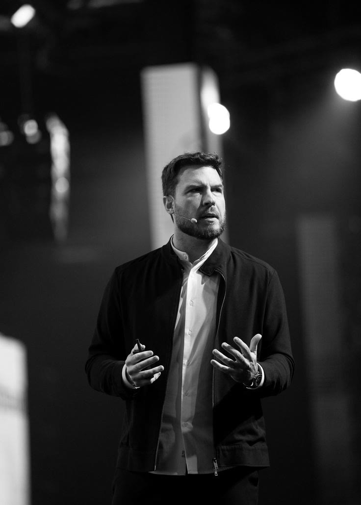 Homem falando no palco de um evento, em preto e branco
